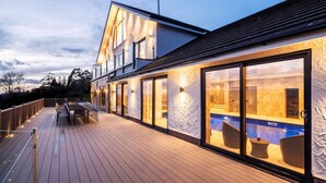 Une maison moderne dotée d’une terrasse en bois, de grandes portes-fenêtres coulissantes et d’une piscine visible à travers les fenêtres.