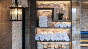 Un espace d’accueil avec un mur en pierre, un luminaire suspendu et des étagères où sont exposées des serviettes et des paniers.