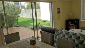 Une pièce dotée d’une porte-fenêtre coulissante donnant sur un patio, d’un canapé, d’une table avec un set de table et d’un meuble contenant une lampe et des objets décoratifs.