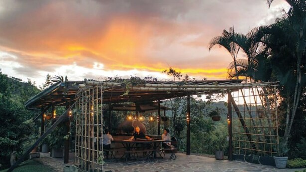 An outdoor dining area with a rustic pergola structure, stone flooring, and potted plants. - QUEBRADAHONDA ESTATE (La Vega)