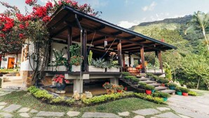 A house with a wooden porch, potted plants, and a stone pathway leading to the entrance. - QUEBRADAHONDA ESTATE (La Vega)