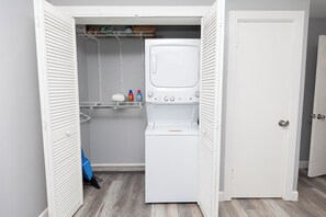 Un lavadero con lavadora y secadora, estantes con productos de limpieza y una puerta.