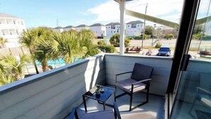 Un balcón con una mesa de vidrio y dos sillas, con vista a una zona residencial con palmeras y casas.