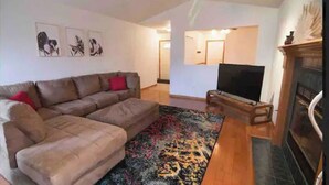 A living room with a sectional sofa, a flat-screen TV, a fireplace, and a patterned rug. - •Vibrant 4 bedroom house 2 king beds in Ankeny• (Ankeny)