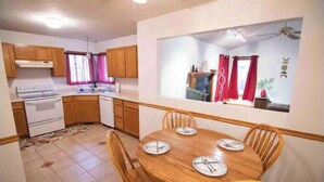 A compact kitchen with wooden cabinets, a stove, and a dining table with chairs. - •Vibrant 4 bedroom house 2 king beds in Ankeny• (Ankeny)