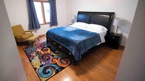 A bedroom with a bed, a chair, a nightstand, a lamp, and a window with curtains. - •Vibrant 4 bedroom house 2 king beds in Ankeny• (Ankeny)