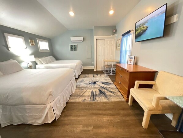 Une chambre d’hôtel avec deux lits, un plancher en bois, un bureau, une chaise, une commode, une télévision et une fenêtre.