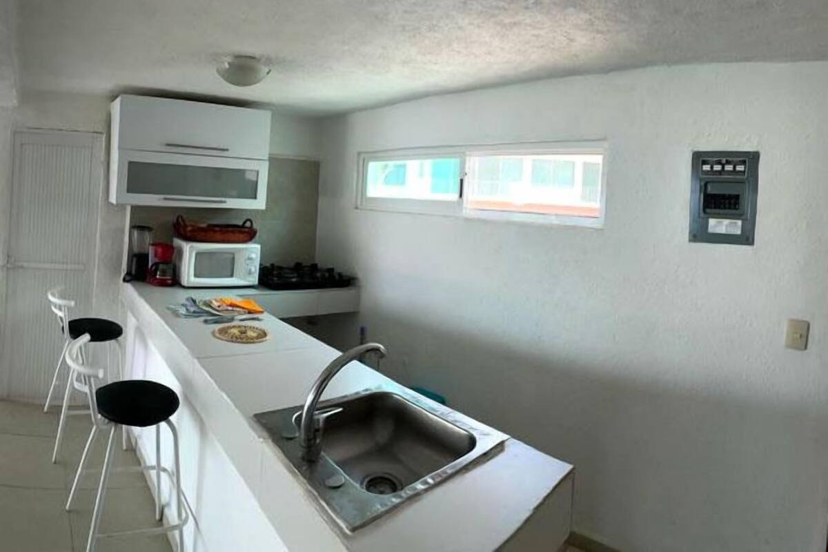 Cocina compacta con encimera blanca, un lavamanos y una ventana arriba.