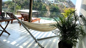 A hammock under a pergola with a view of a coastal area, a table with chairs, and a potted plant. - El acantilado (Acapulco)