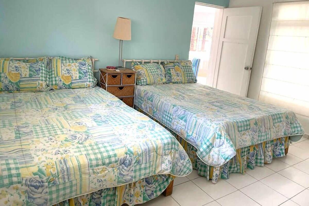Una habitación con dos camas, una mesita de noche y un ventanal con cortinas.
