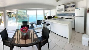 A modern kitchen with a large island, white cabinets, and a view of the ocean. - El acantilado (Acapulco)