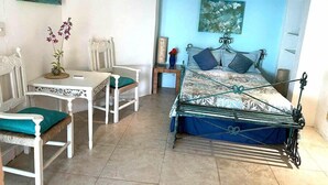 A bedroom with a bed, two chairs, a table, and a painting on the wall. - El acantilado (Acapulco)