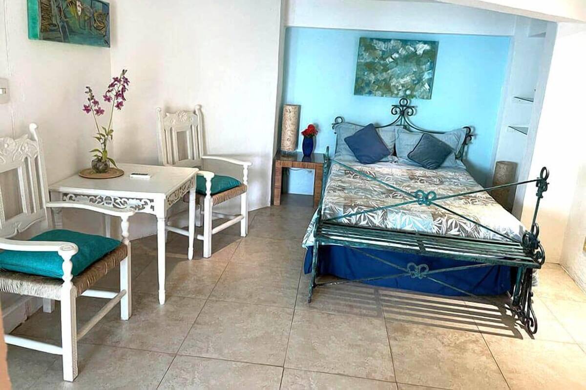 Un dormitorio con cama, dos sillas, una mesa y un cuadro en la pared.