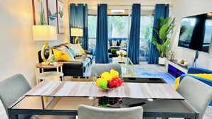 A modern living room with a dining area, featuring a sofa, a TV, and a dining table with fruit. - Newly updated Modern 2 BR  Scottsdale Condo. (Scottsdale)