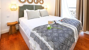A neatly made bed with a patterned blanket, a bedside table with a lamp, and decorative wall mirrors. - Offline Mood Apartment (Faro)