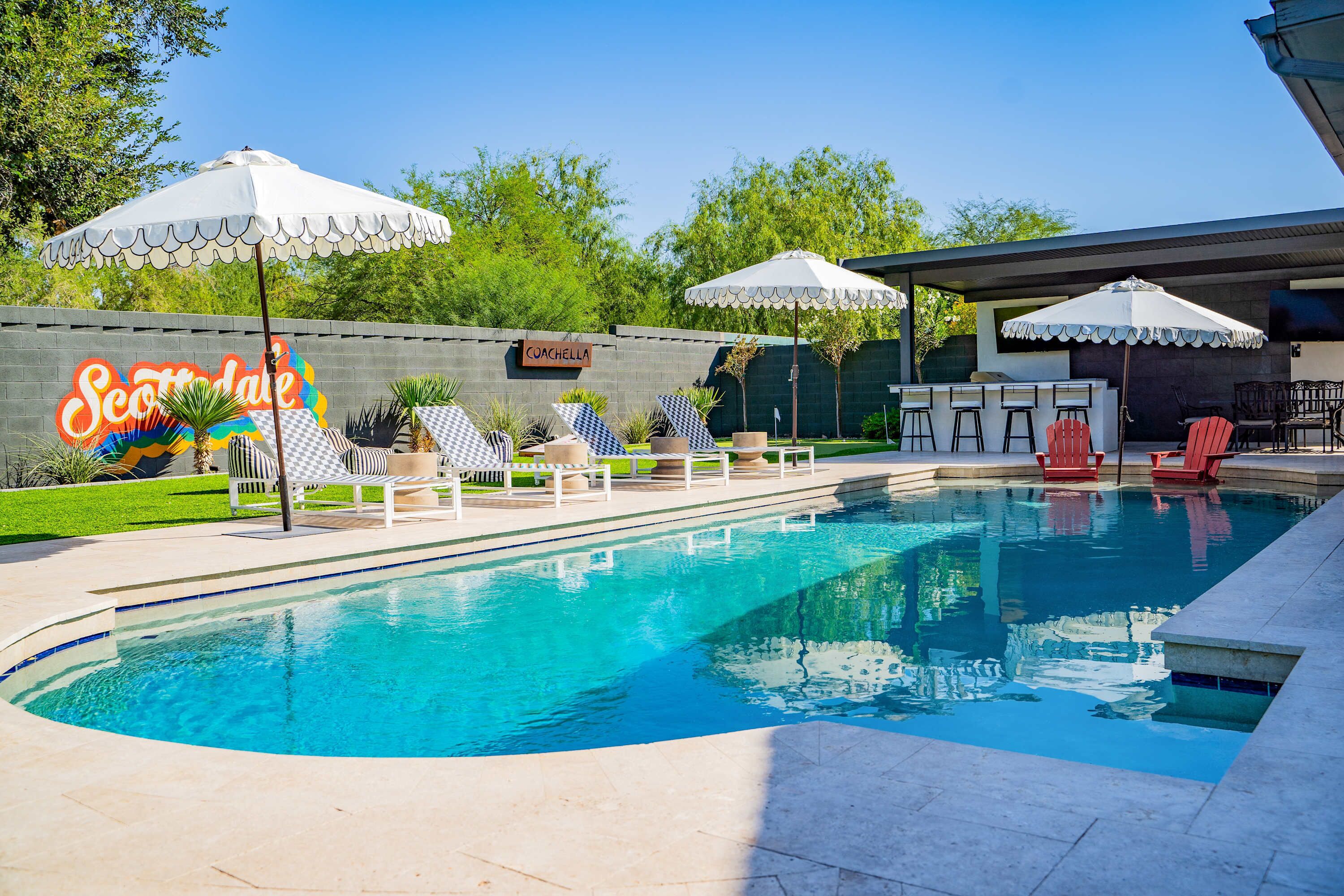 Une piscine avec des chaises longues et des parasols, un panneau indiquant « Scottsdale », et un espace bar.