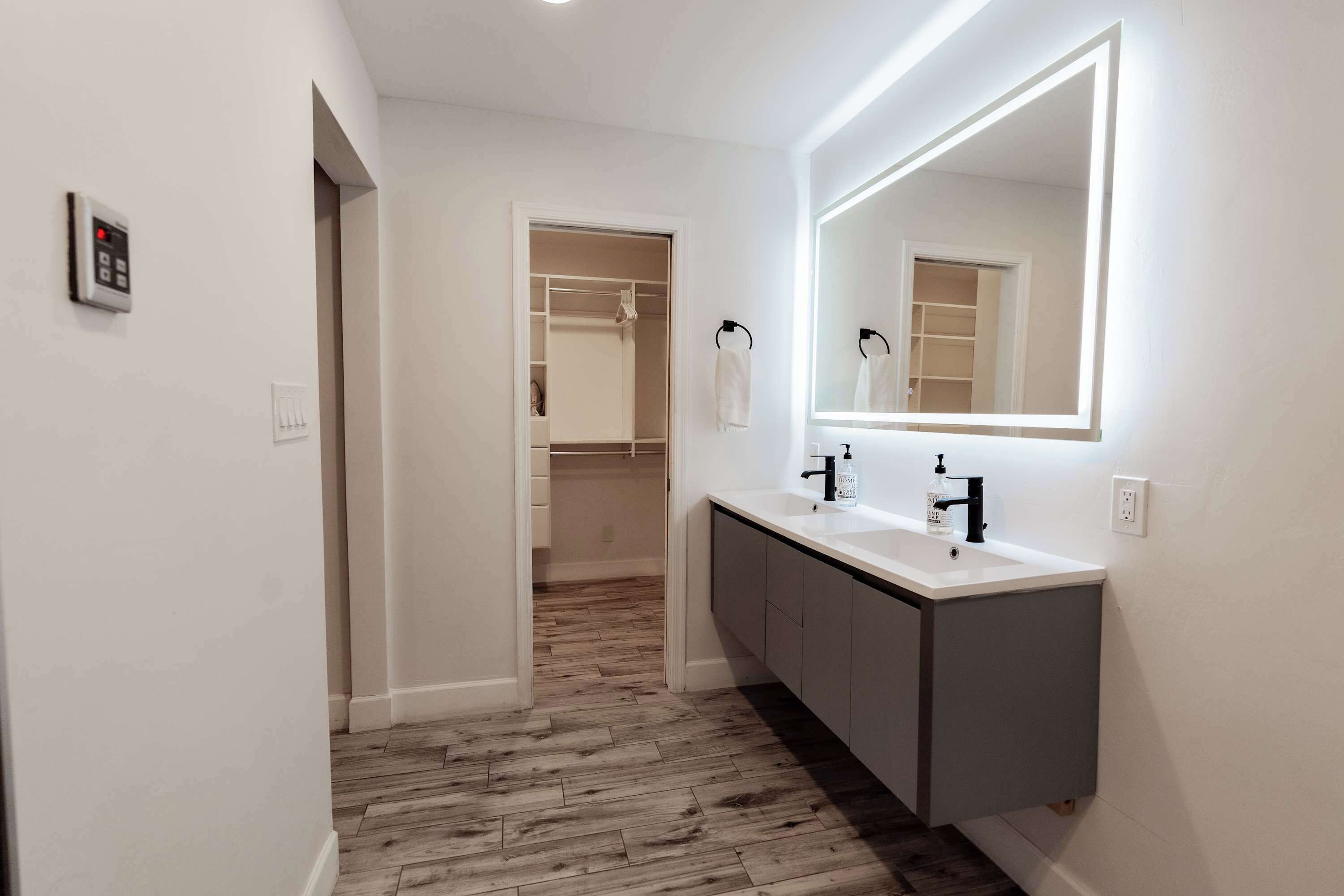 Une salle de bain moderne avec un grand miroir, deux lavabos et un dressing.