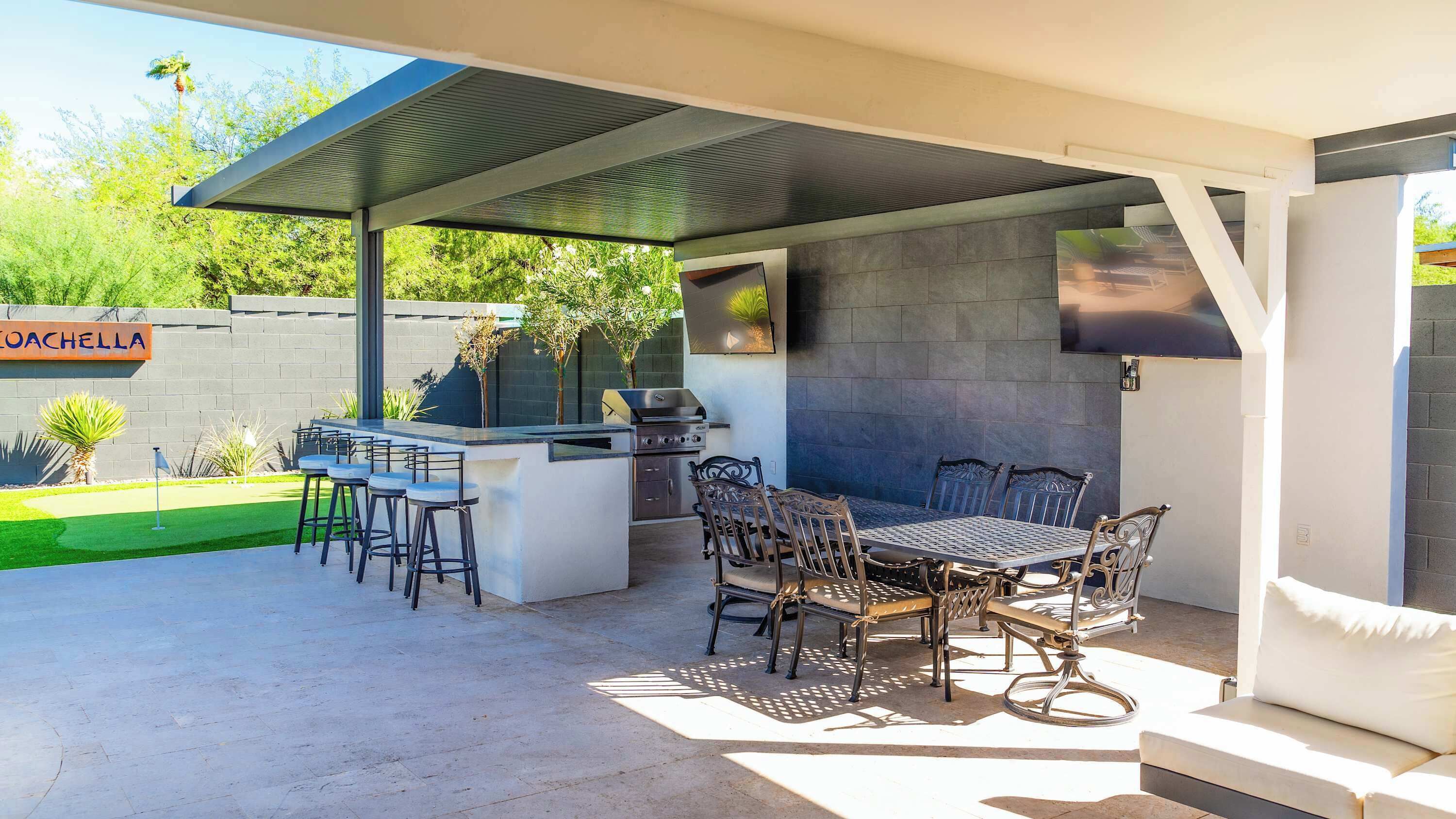 Une terrasse extérieure équipée d’un barbecue, de tabourets de bar et d’une table à manger avec des chaises.
