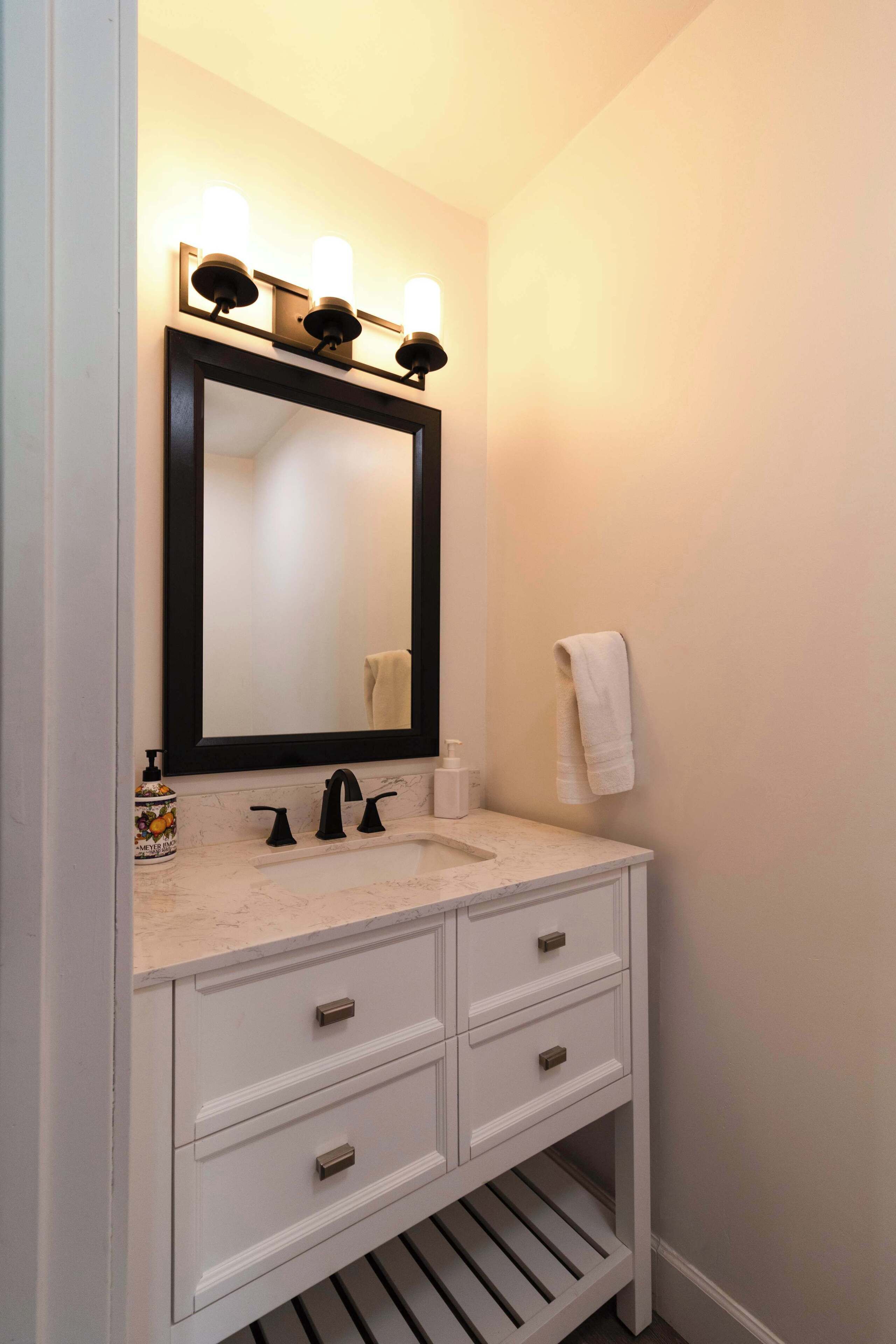 Une salle de bain avec un meuble-lavabo blanc, un robinet noir et un grand miroir agrémenté de trois lampes.