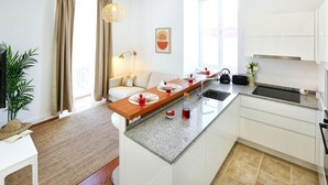 Une cuisine moderne dotée d’un îlot central, de meubles blancs et d’un coin repas comprenant un canapé et une table pour quatre personnes.