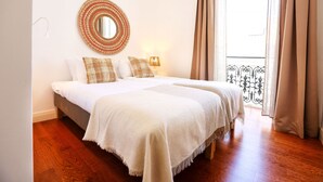 Une chambre avec deux lits, un miroir rond, une lampe et un balcon doté d’une balustrade en fer forgé.