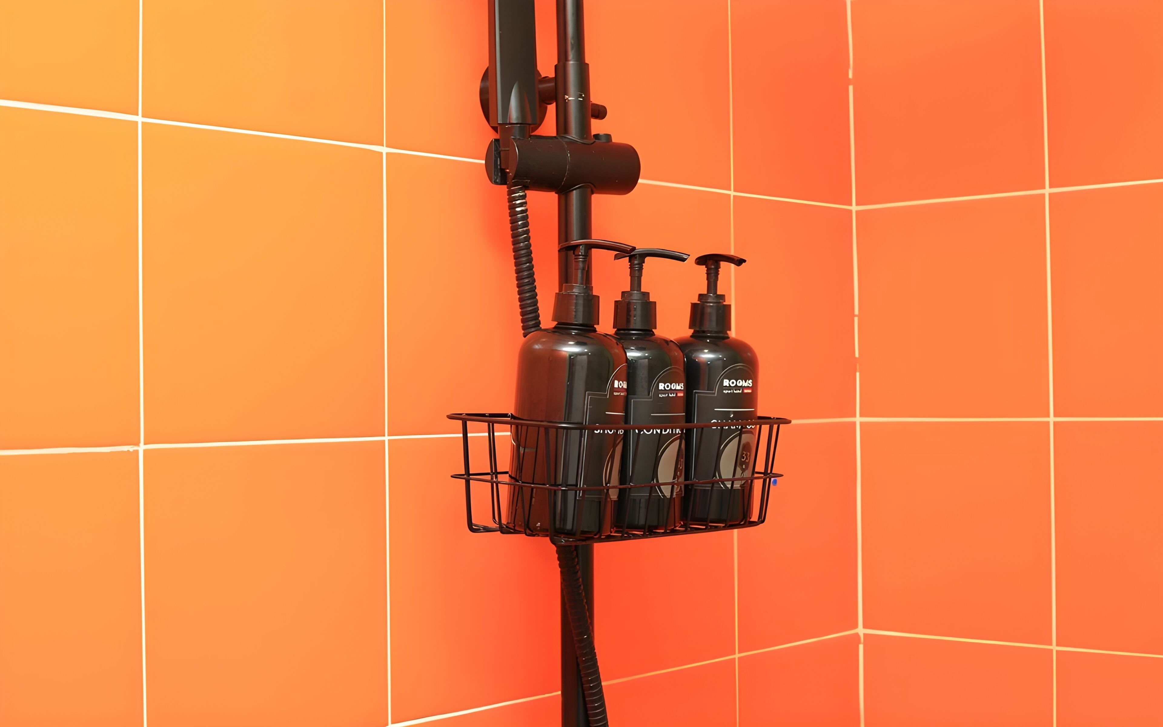 A shower area with a black hose and a metal rack holding three bottles.