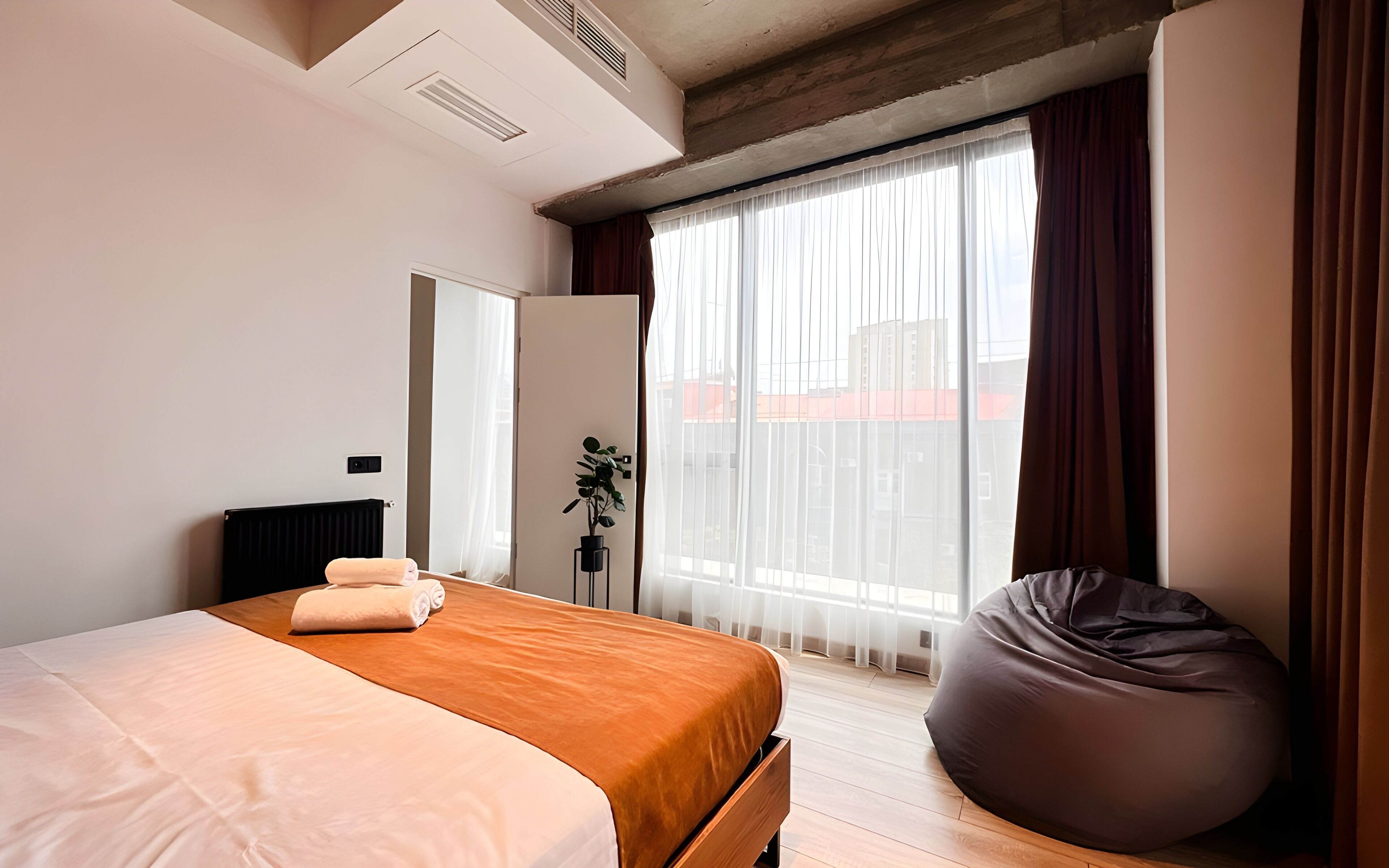 A modern bedroom with a large bed, a wooden headboard, a potted plant, and a bean bag chair.