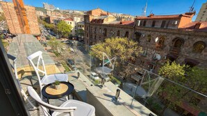 Un balcon avec des chaises blanches et une petite table, d’où l’on peut admirer un paysage urbain avec des bâtiments historiques et un ciel dégagé.