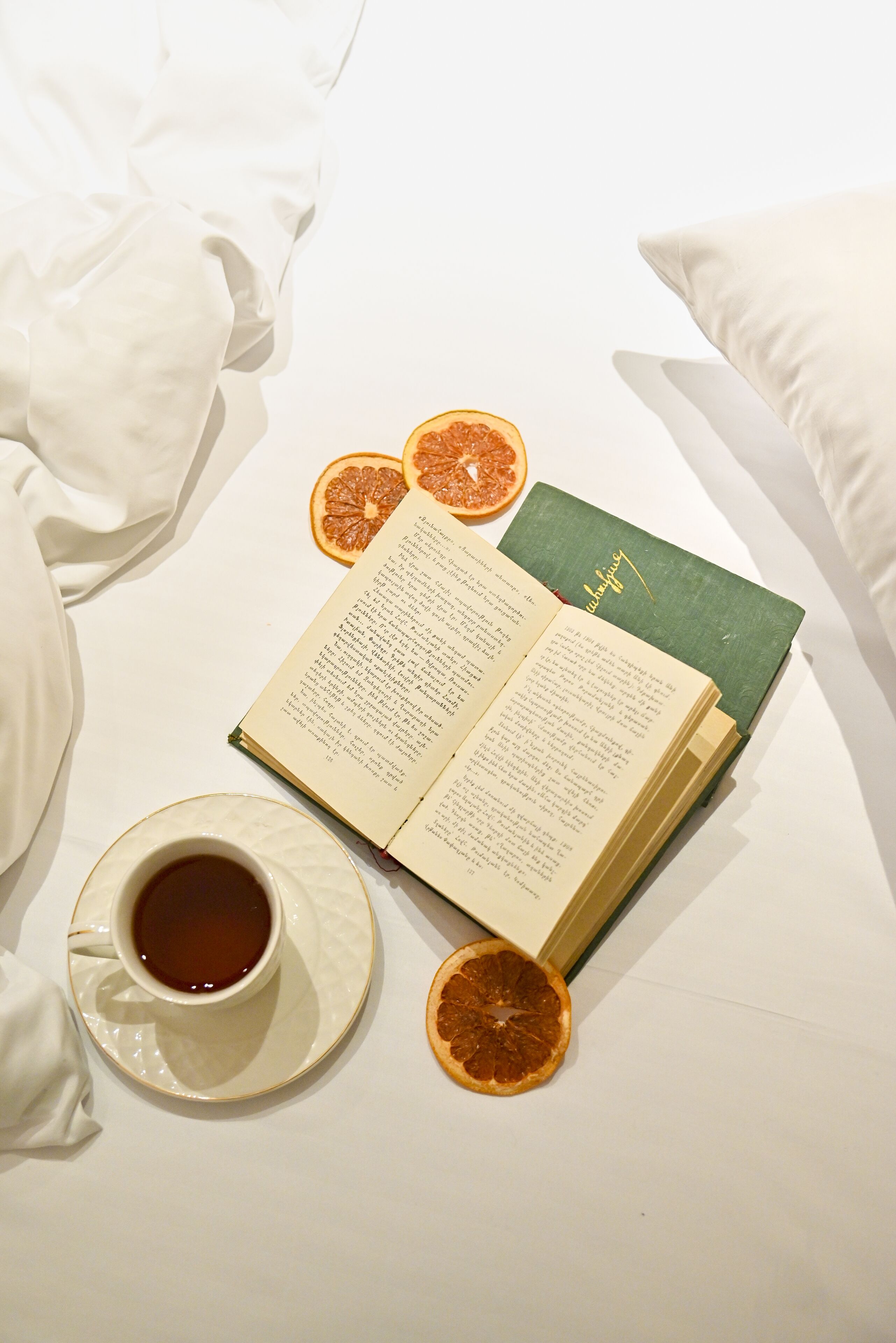 Un libro, una taza de té y rodajas de naranja deshidratada sobre una superficie blanca.