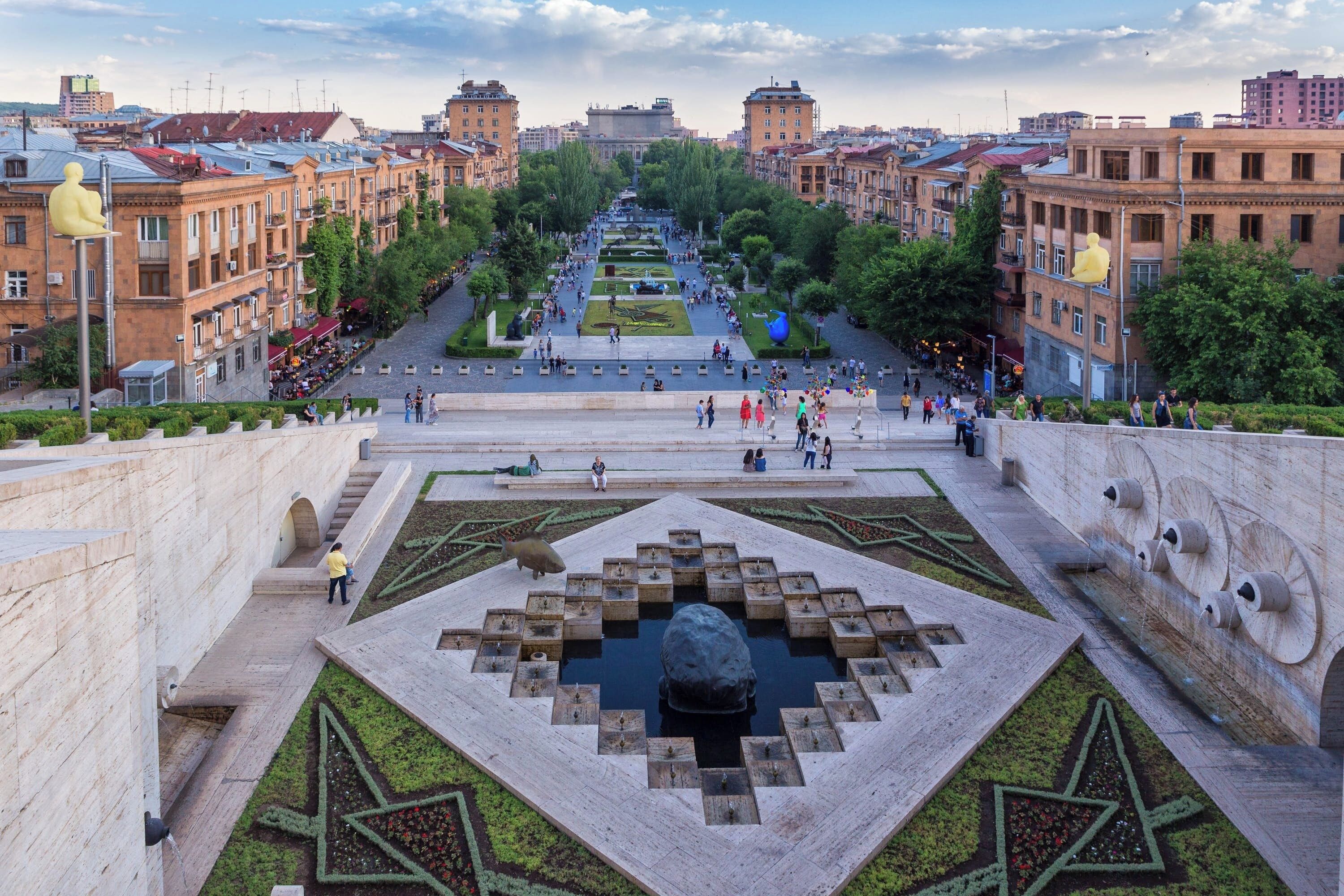 A spacious square with a central fountain, surrounded by well-maintained gardens and historic buildings.