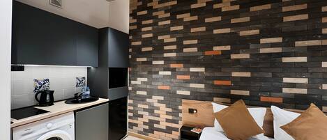 Habitación de hotel compacta con cocina moderna, lavadora y cama con almohadas marrones.