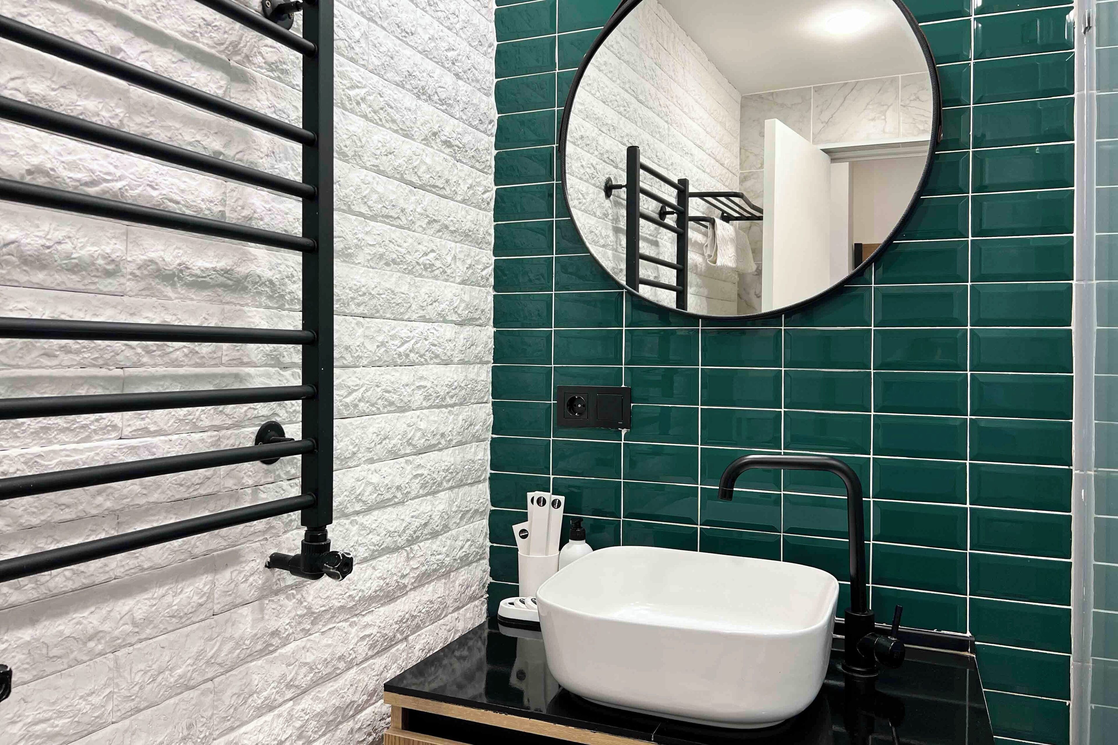 Une salle de bain avec un lavabo blanc, un robinet noir et un miroir rond.
