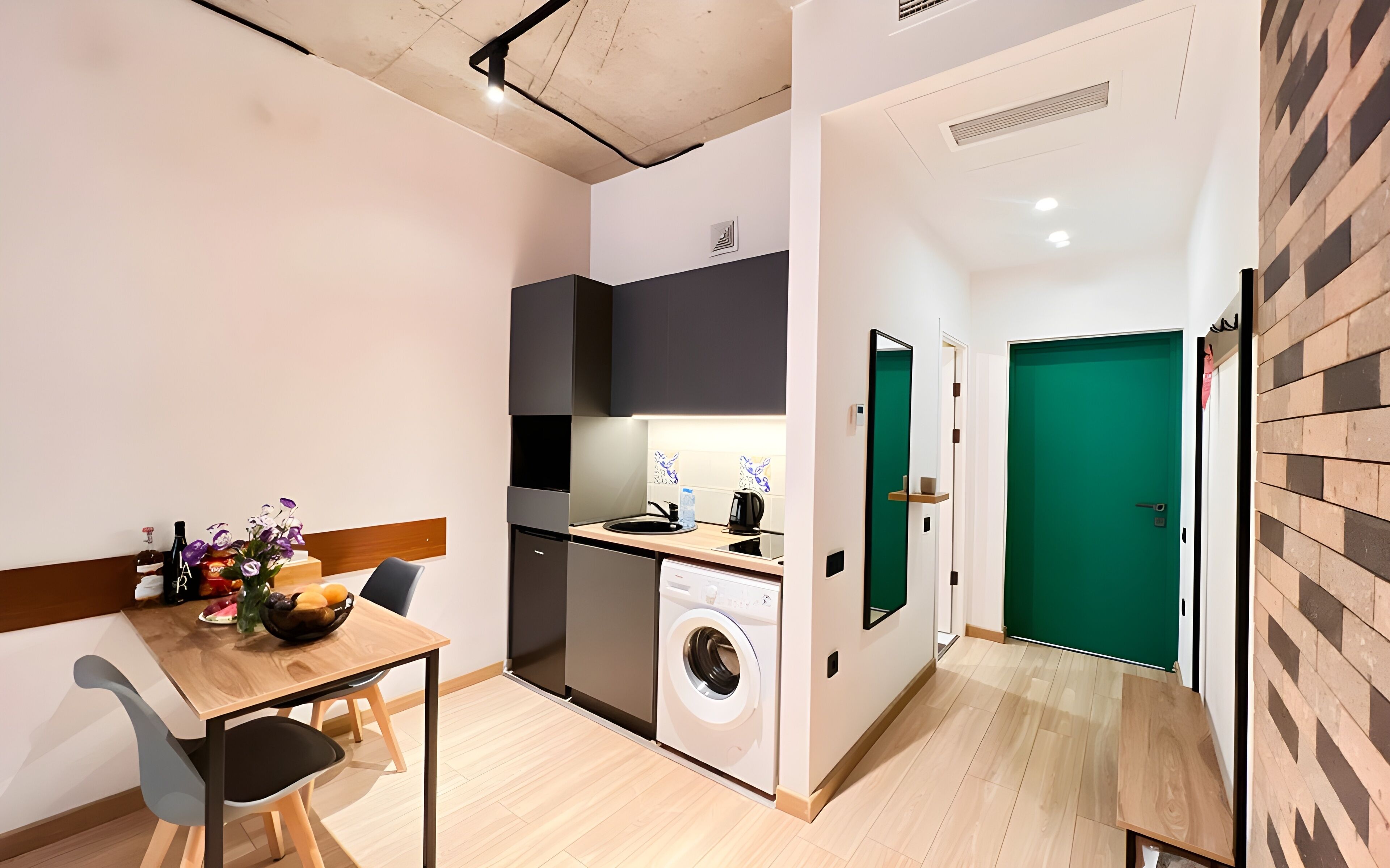 A compact kitchen with a washing machine, a dining area with a table and chairs, and a green door.