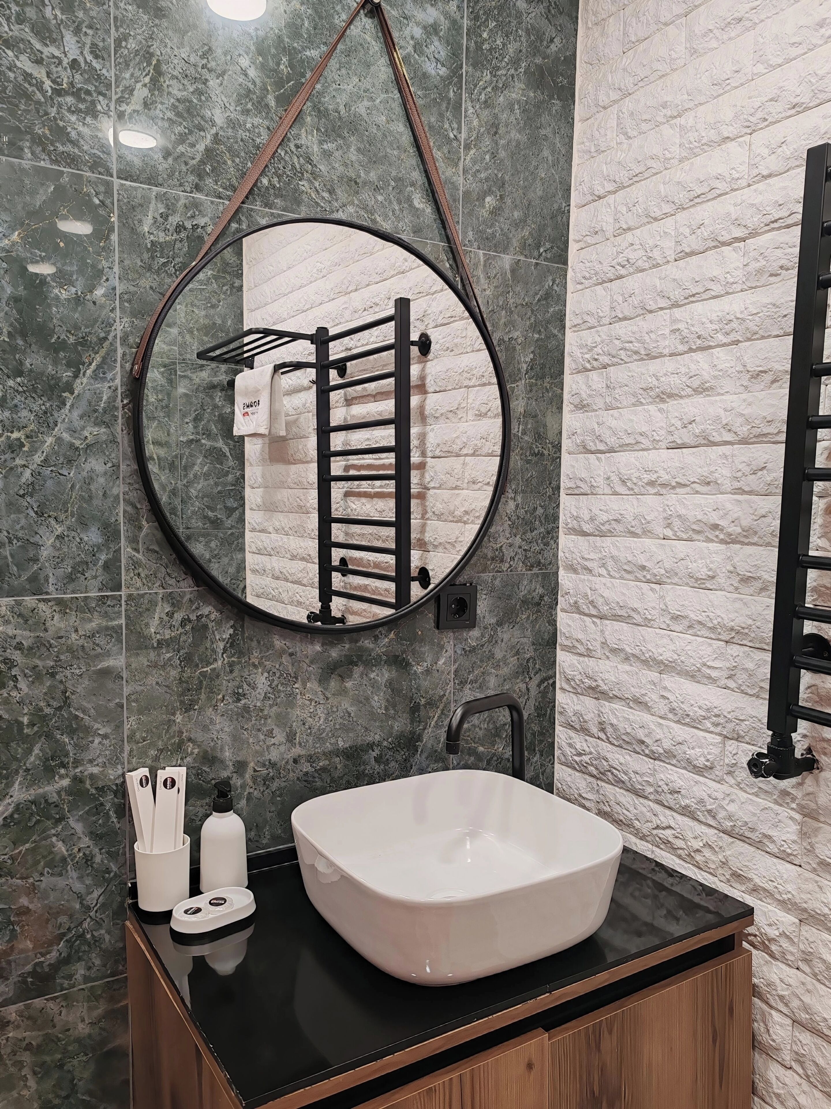 Un baño con un espejo redondo, toallero, lavamanos y un armario de madera.