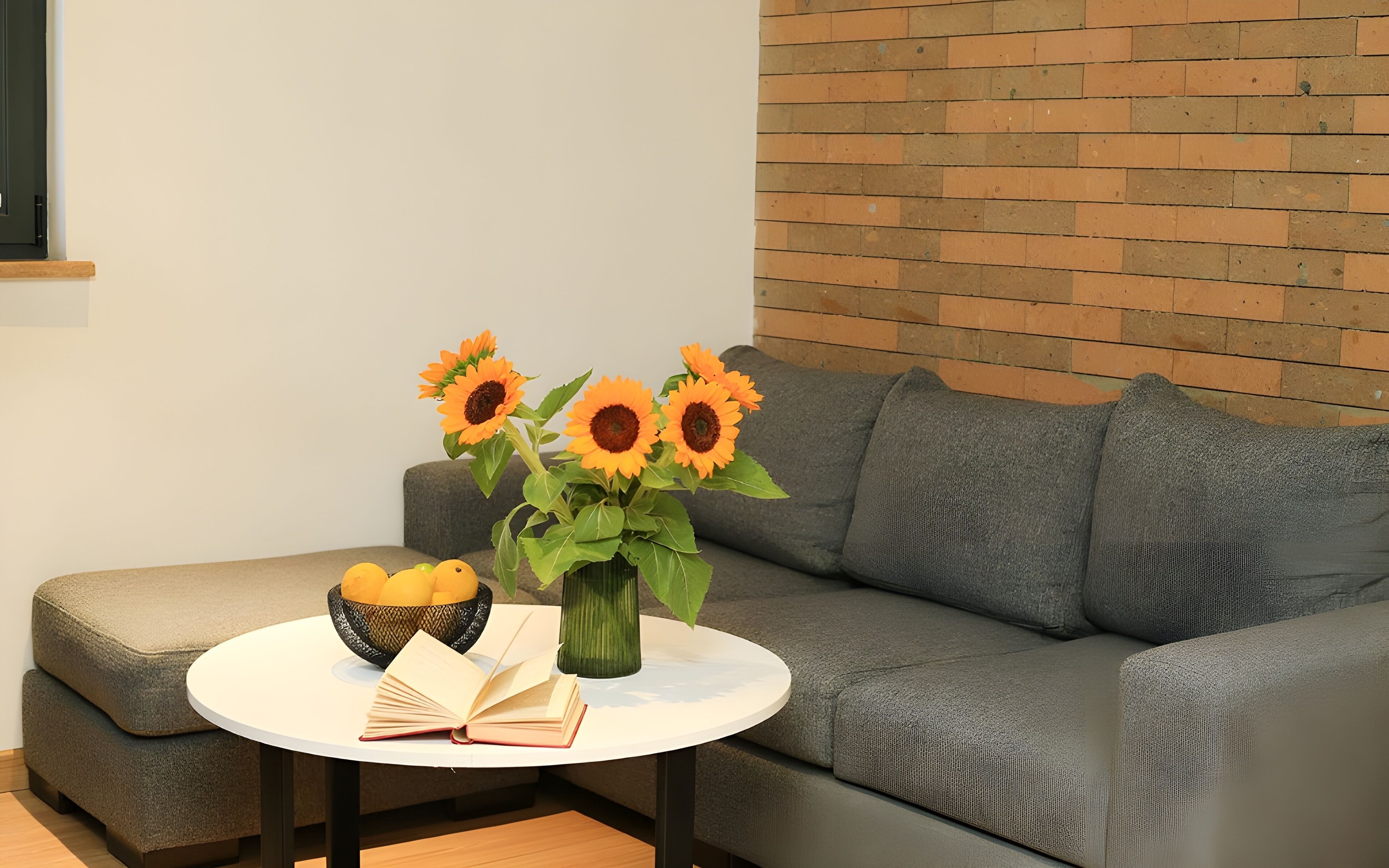 Una sala de estar moderna con un sofá gris, una mesa de centro redonda blanca, un jarrón con girasoles, un cuenco de limones y un libro.