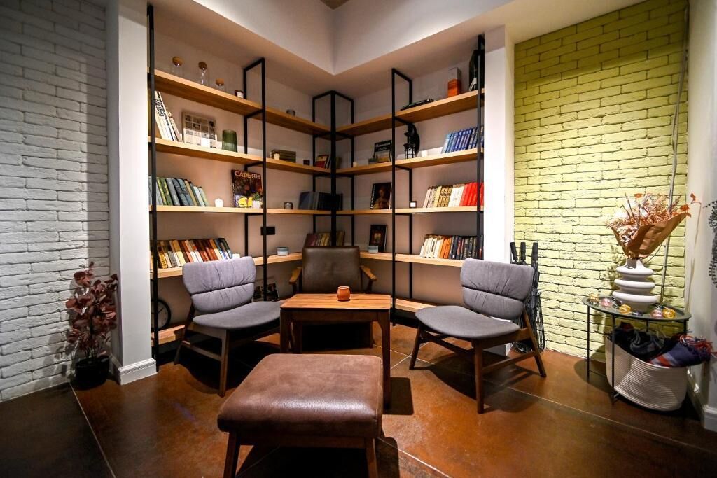 Un rincón acogedor para leer, con una estantería, dos sillones, una mesita y un reposapiés de cuero.
