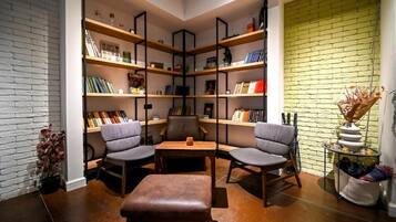 Un rincón acogedor para leer, con una estantería, dos sillones, una mesita y un reposapiés de cuero.