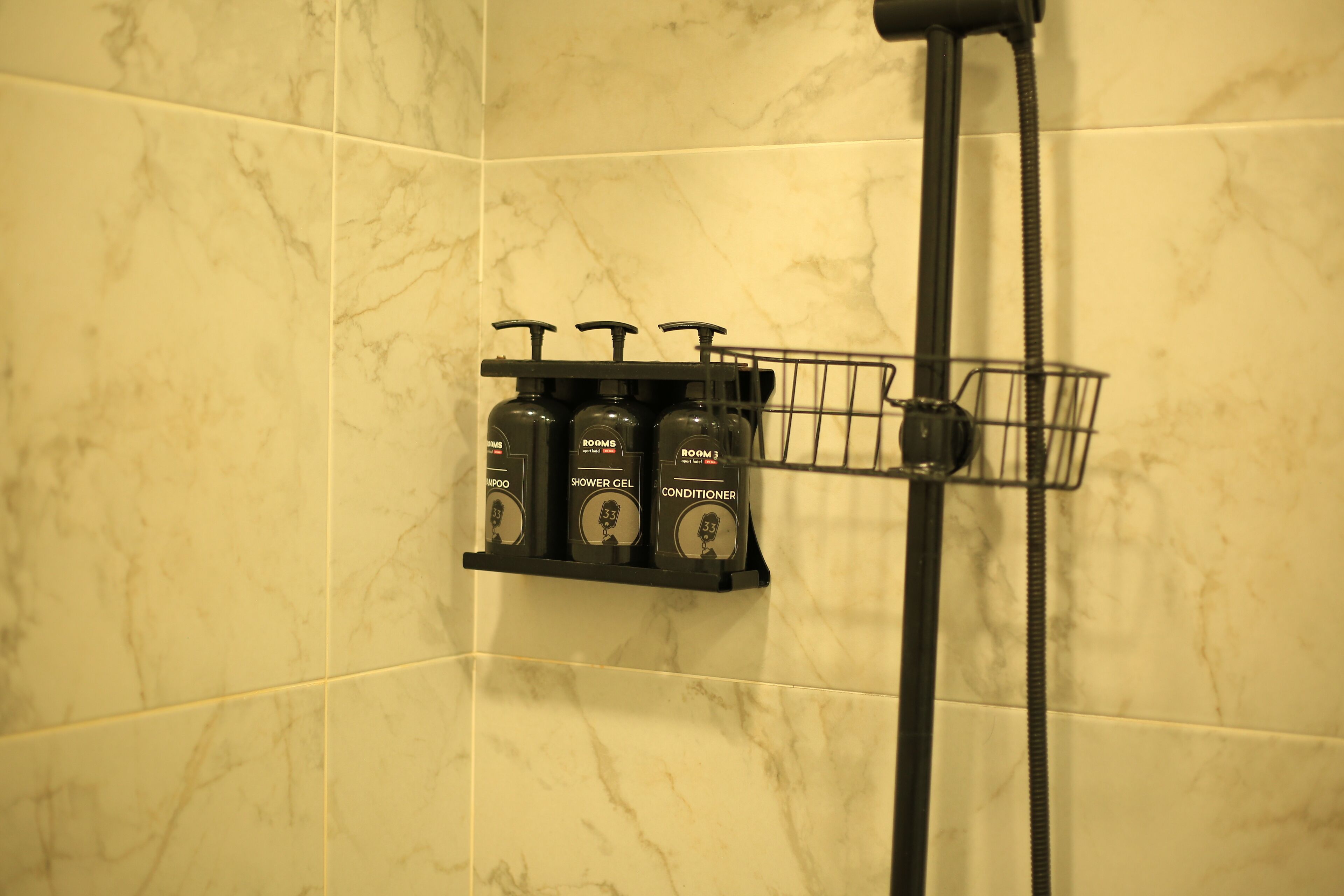 A bathroom with a marble wall and a shelf holding three bottles labeled "Shower Gel," "Shower Gel," and "Conditioner."