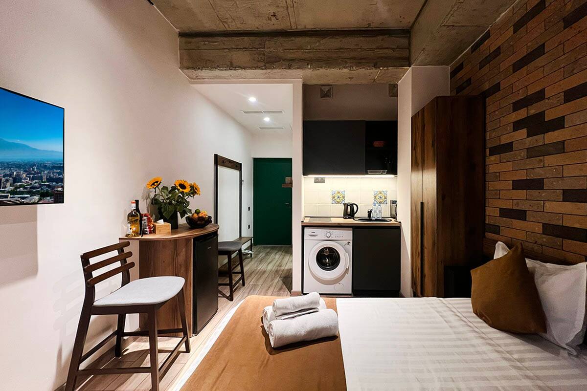 Quarto de hotel compacto com cama, secretária de madeira, máquina de lavar roupa e vista para a cidade.