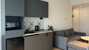 Ett modernt kök med en inbyggd mikrovågsugn, ett Hisense-kylskåp och en diskho. I vardagsrummet finns en grå soffa och ett litet runt bord.