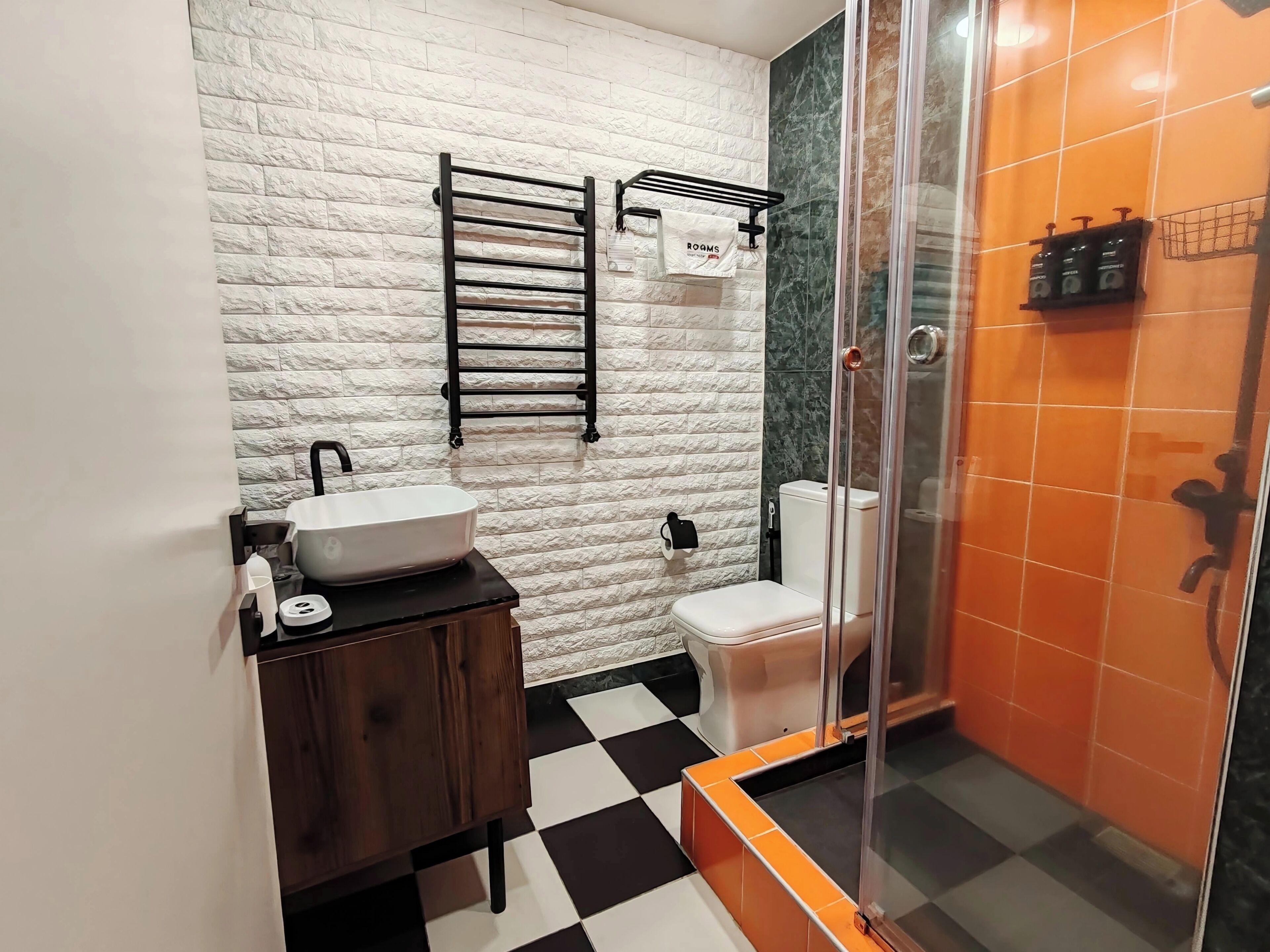 A bathroom with a white textured wall, a black towel rack, a white sink, a toilet, and a glass-enclosed shower area.