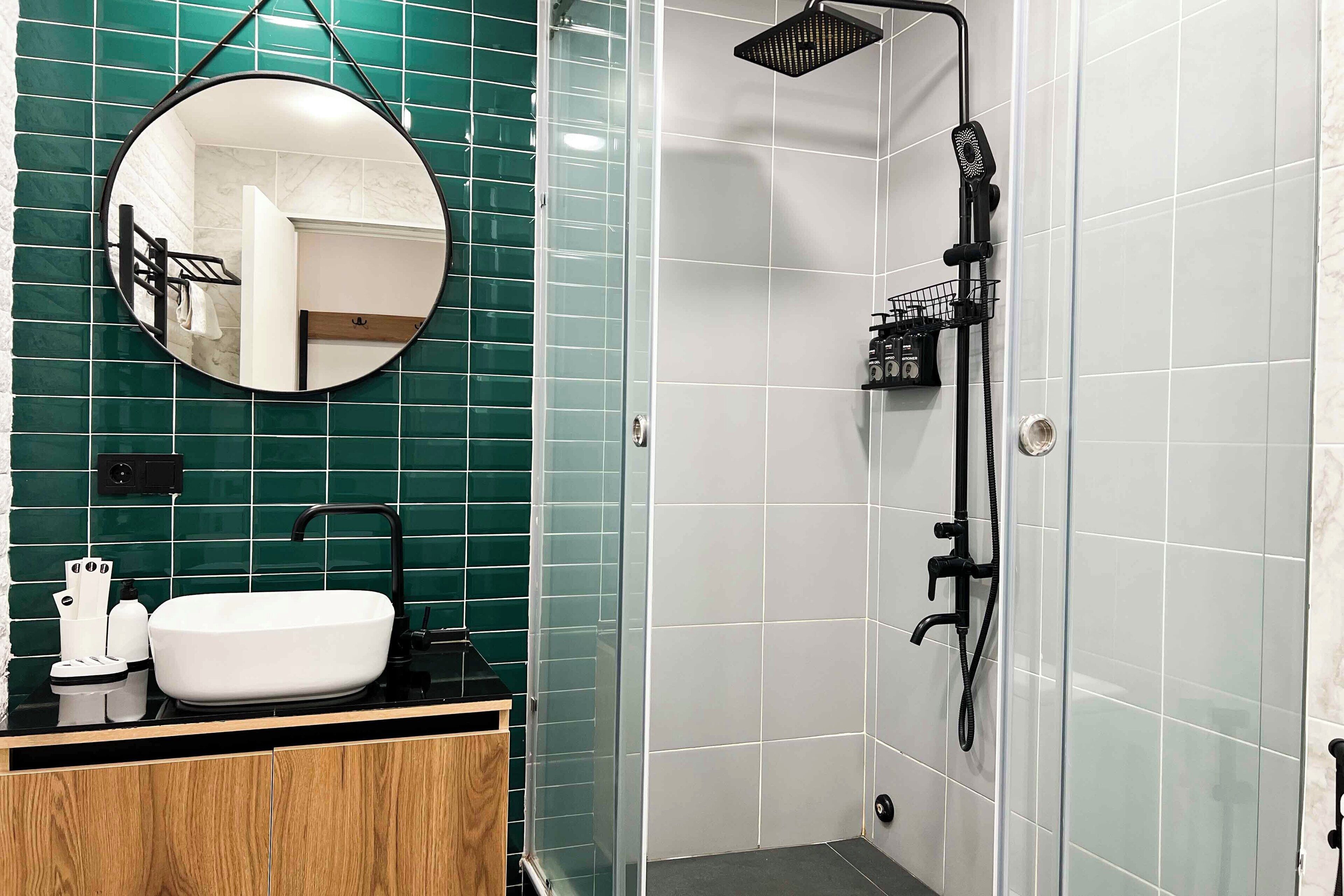 Un baño con un espejo redondo, un lavabo blanco y una zona de ducha con manguera negra.