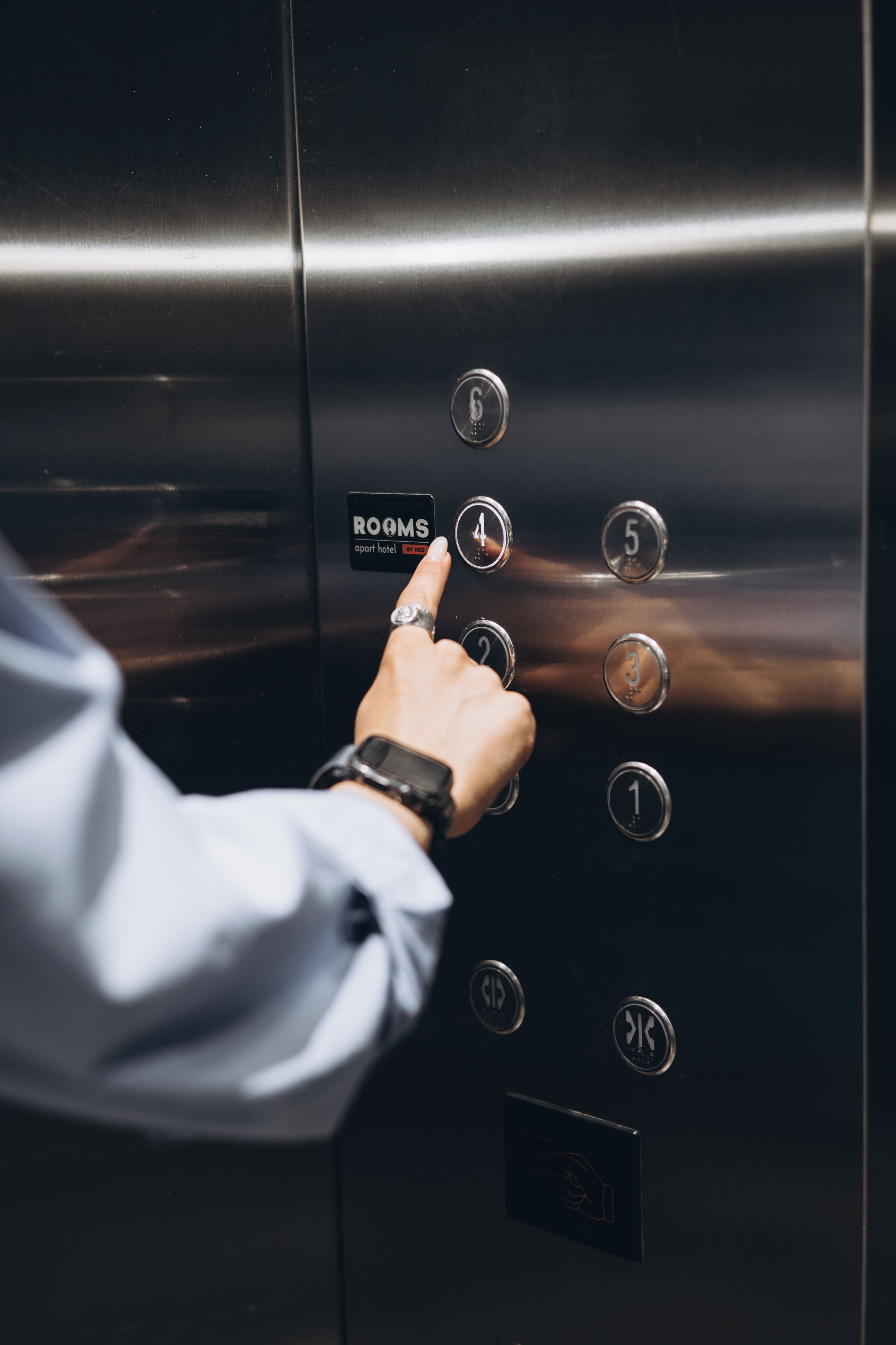 A hand pressing a button on an elevator control panel with room numbers and a 'ROOMS' label.