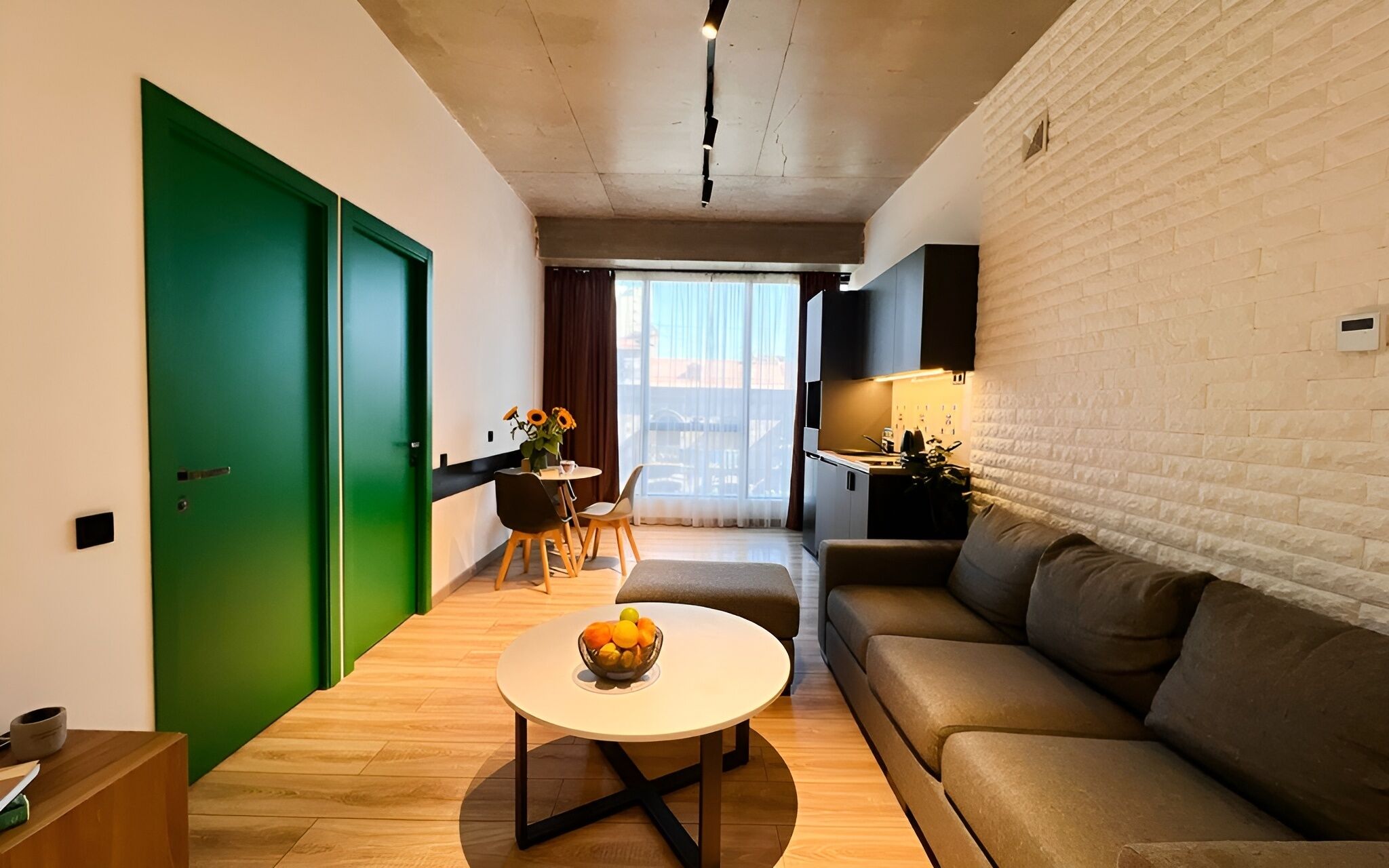 Een moderne woonkamer met een groene deur, een ronde salontafel met fruit, een bank en een eethoek met een tafel en stoelen.