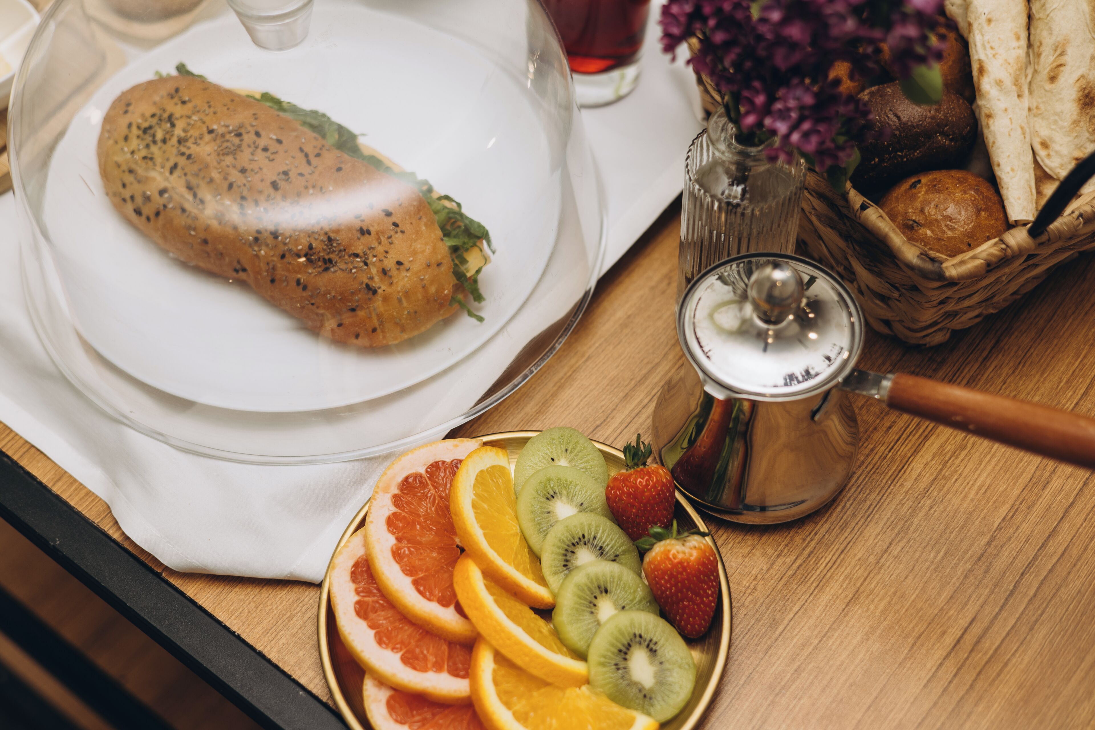 A breakfast setting with a plate of sliced fruits, a loaf of bread, and a coffee pot.