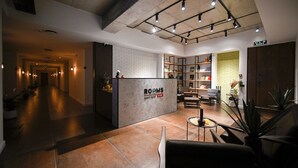 Un hall d’hôtel comprenant un comptoir d’accueil, un espace salon avec une table basse et une bibliothèque.