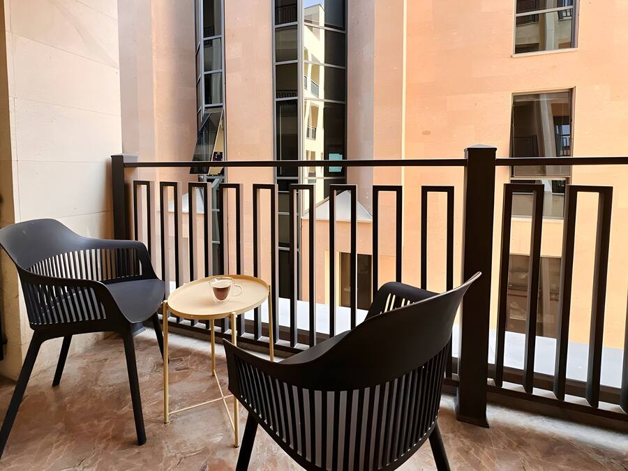 A balcony with two black chairs and a small round table with a cup, surrounded by a black metal railing.