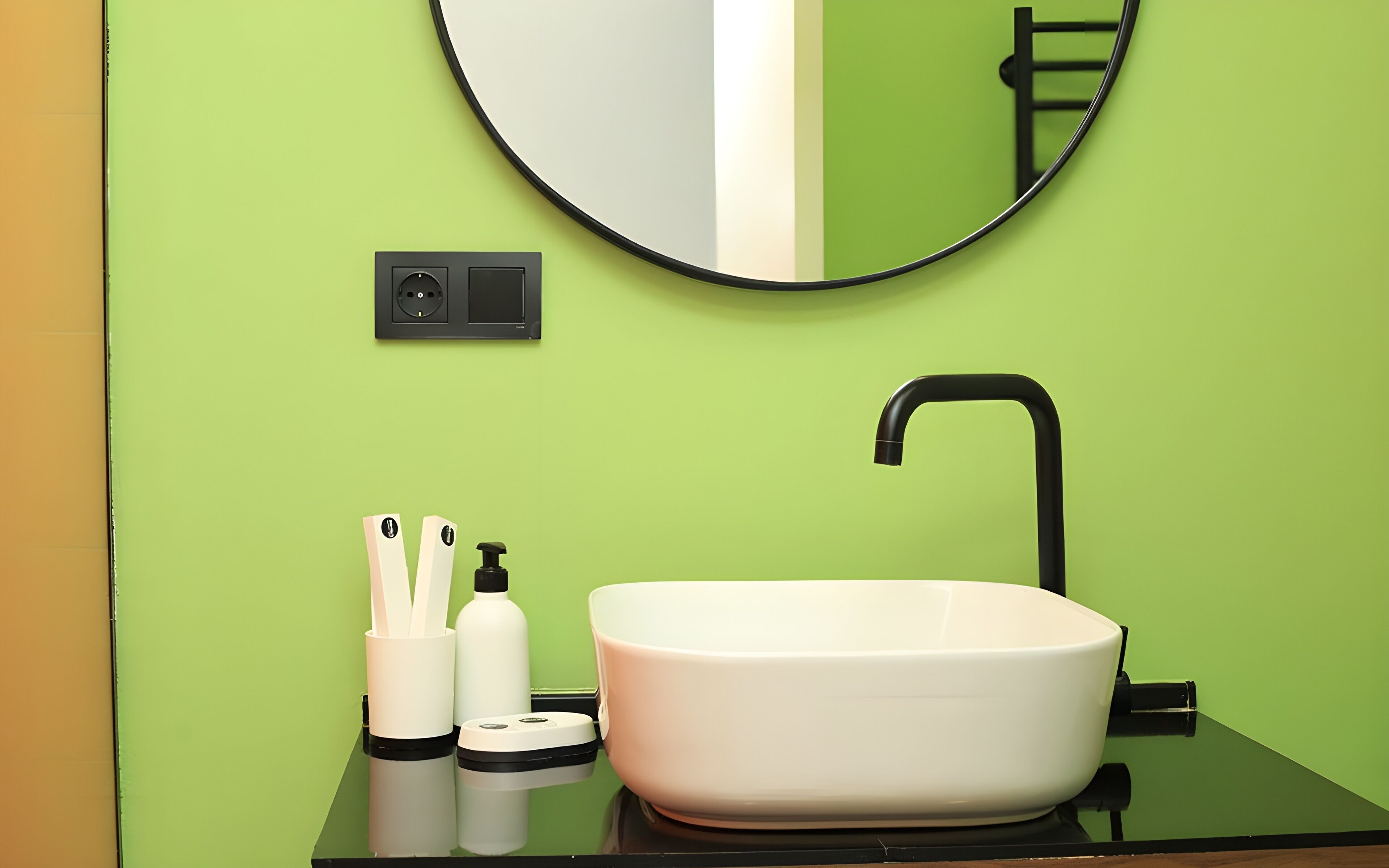Une salle de bain avec un lavabo blanc, un robinet noir et des murs verts.