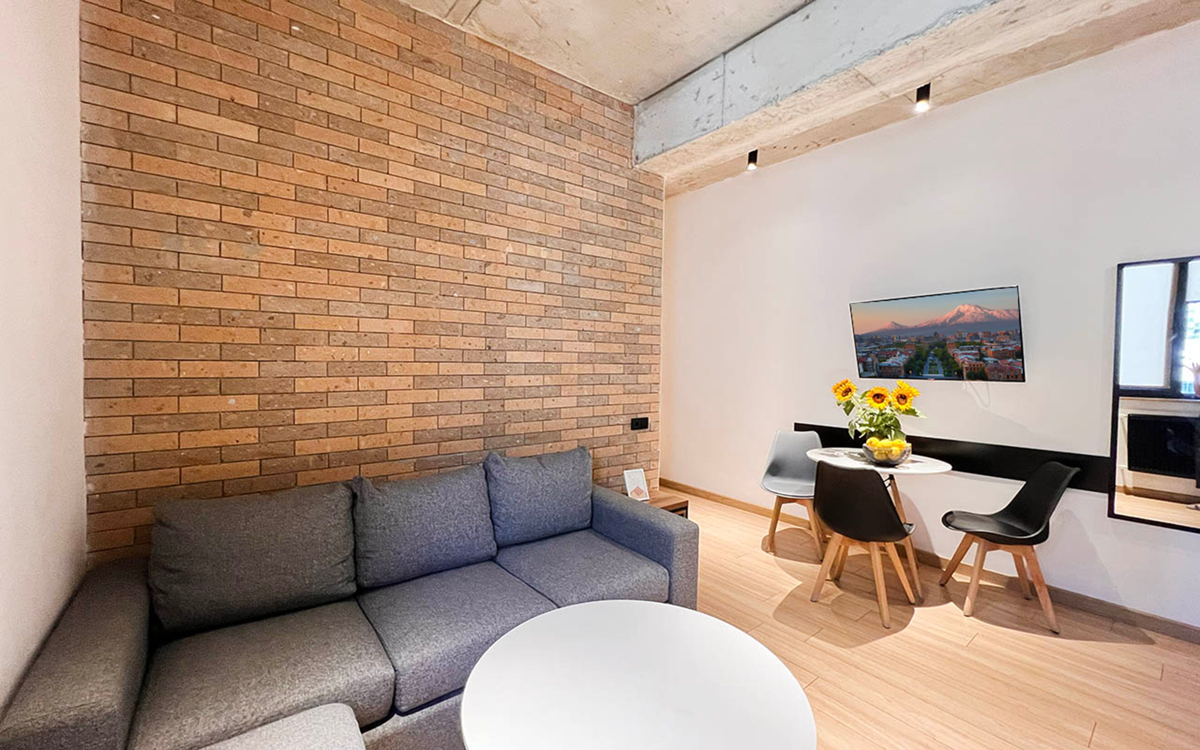 A modern living room with a grey sofa, a round white table, and a dining area with two chairs.