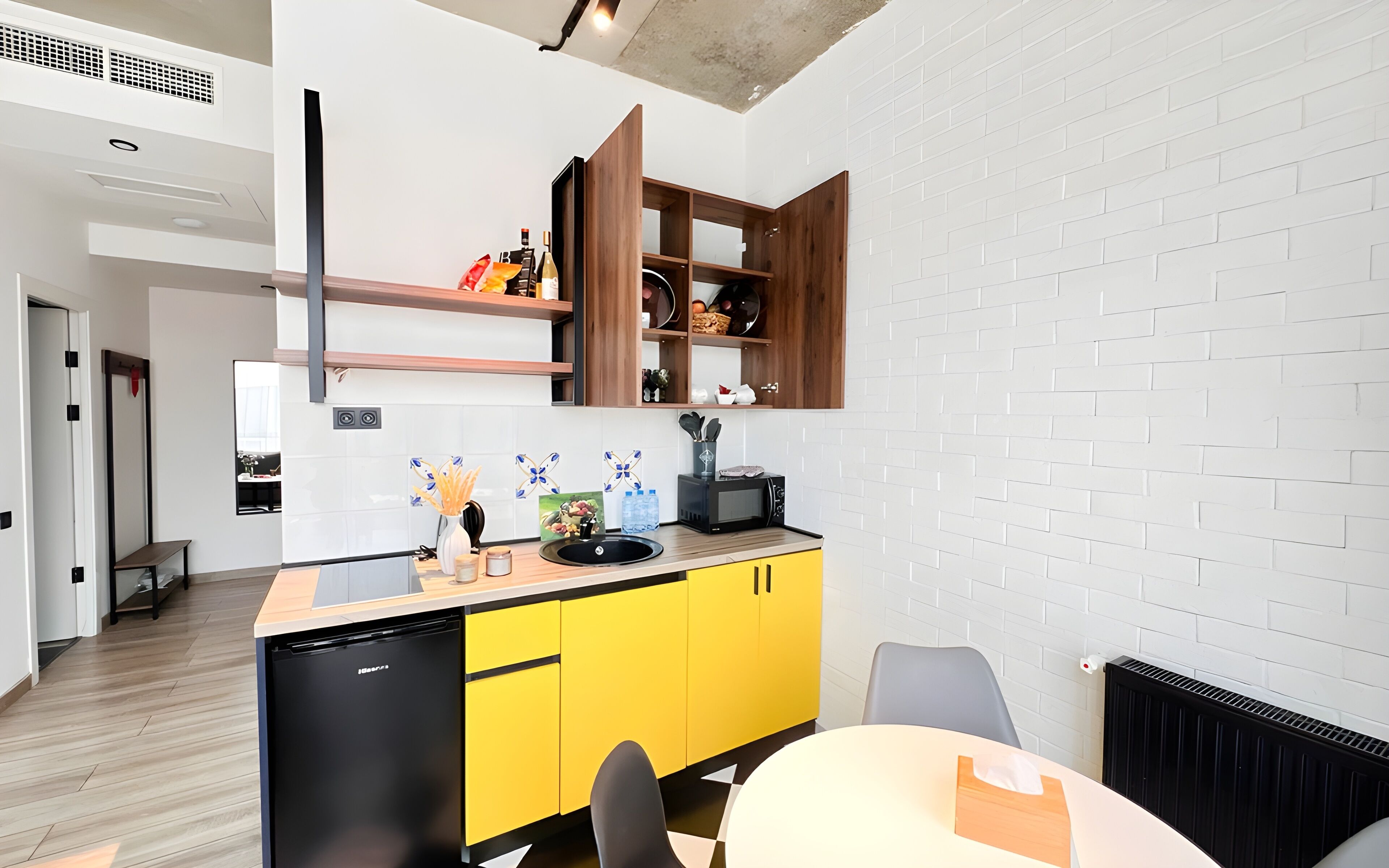 A modern kitchen with a yellow and black color scheme, white brick walls, and a built-in microwave.